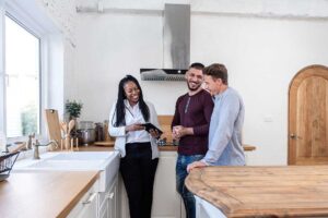 A home inspector examines a residential kitchen sink and plumbing with a flashlight and checklist.